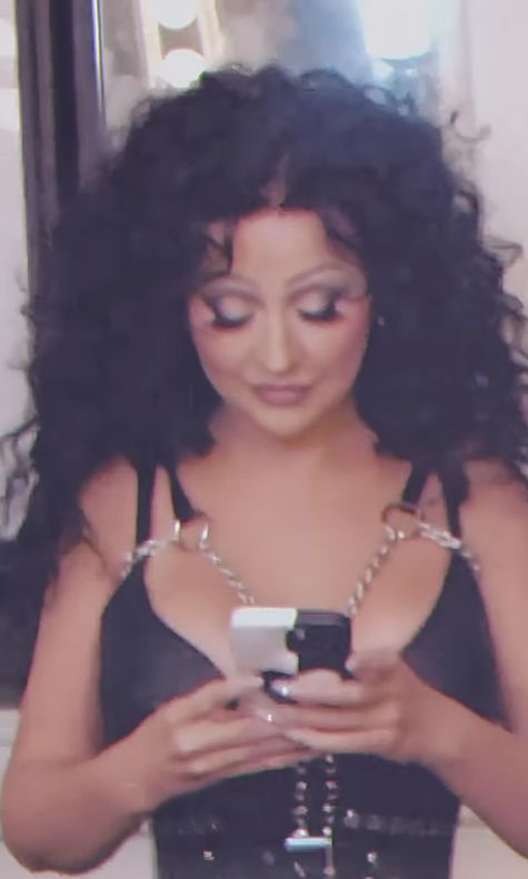 Christina Aguilera dressed as Cher looking at her cell phone