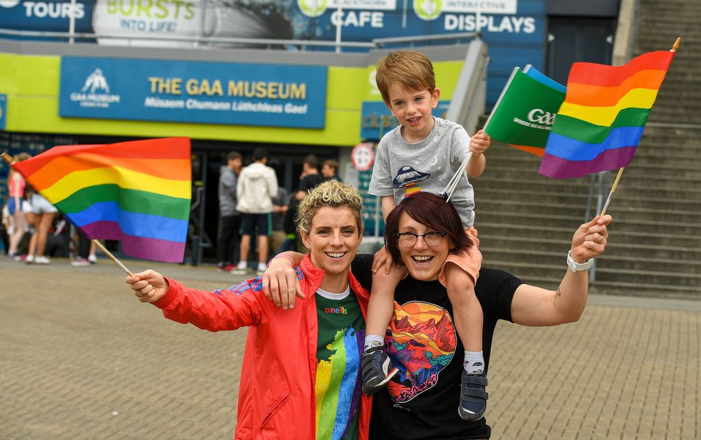 Two women with a boy on their shoulders waving Pride flags