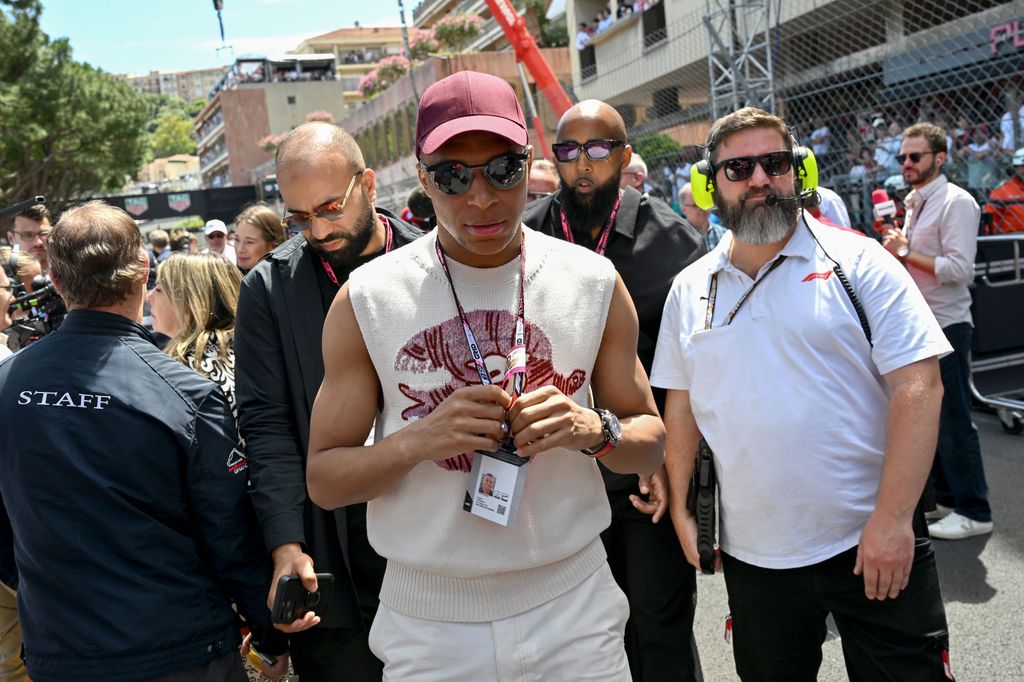 Kylian Mbappe en un libro que usa chaleco impreso, jergas y gorra