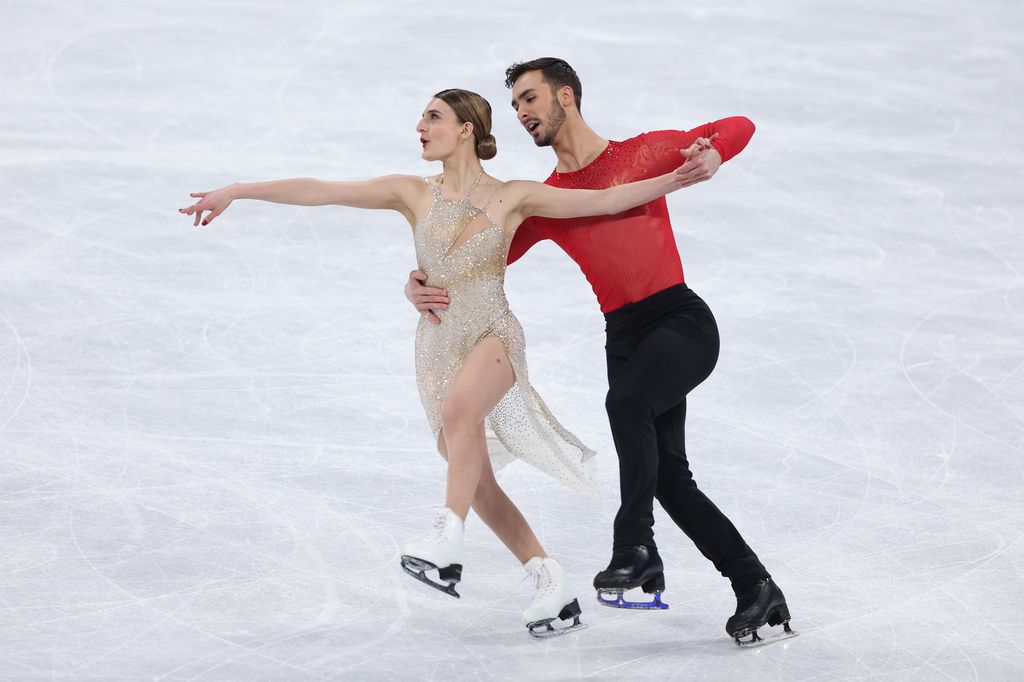   Gabriella Papadakis portant une tenue argentée scintillante et Guillaume Cizeron portant un haut rouge et un pantalon noir, tenant son partenaire par la taille sur la glace  