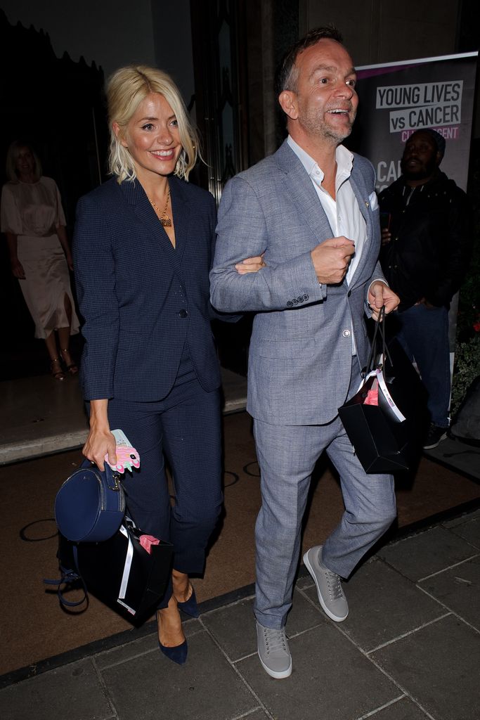 Holly Willoughby and Dan Baldwin in blue suits linking arms as they leave Claridge's Hotel in 2019