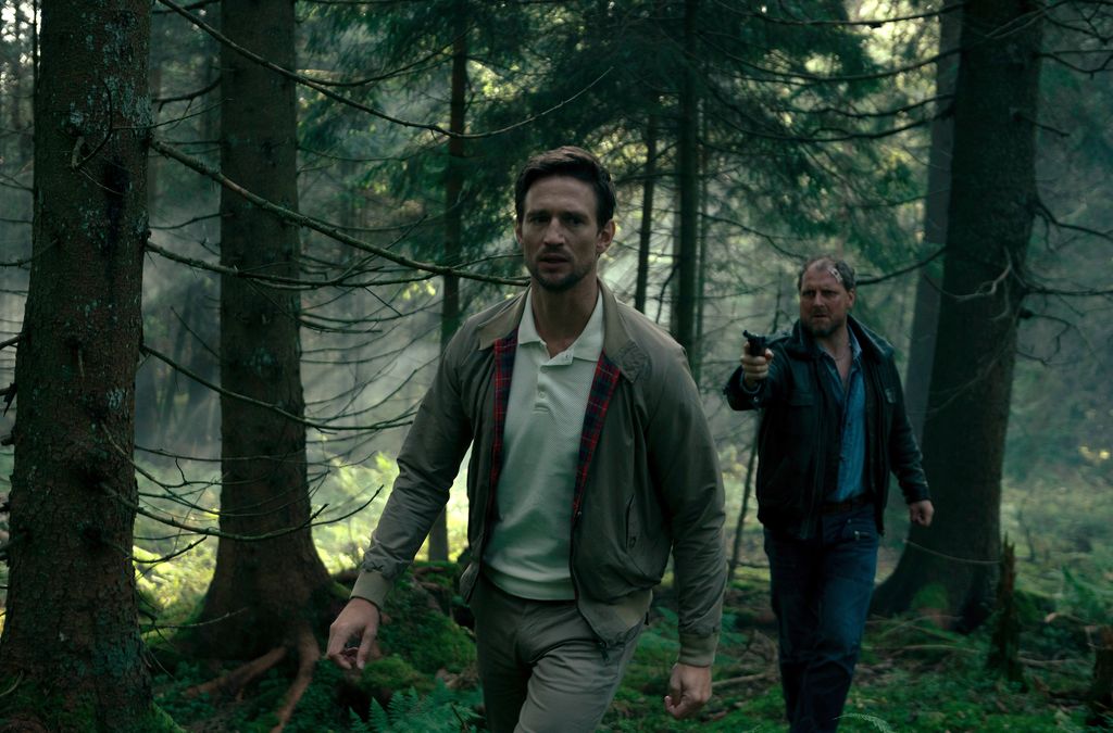 man holding gun to another man in woods