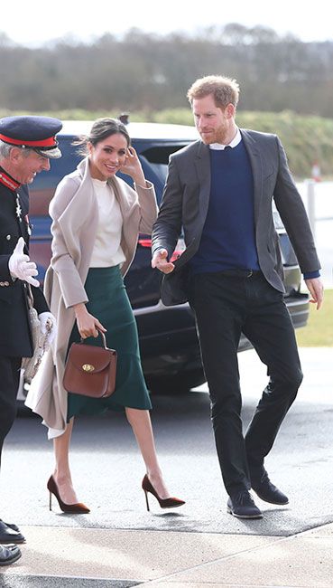 meghan and harry walking on a windy day outside being escorted by man wearing uniform