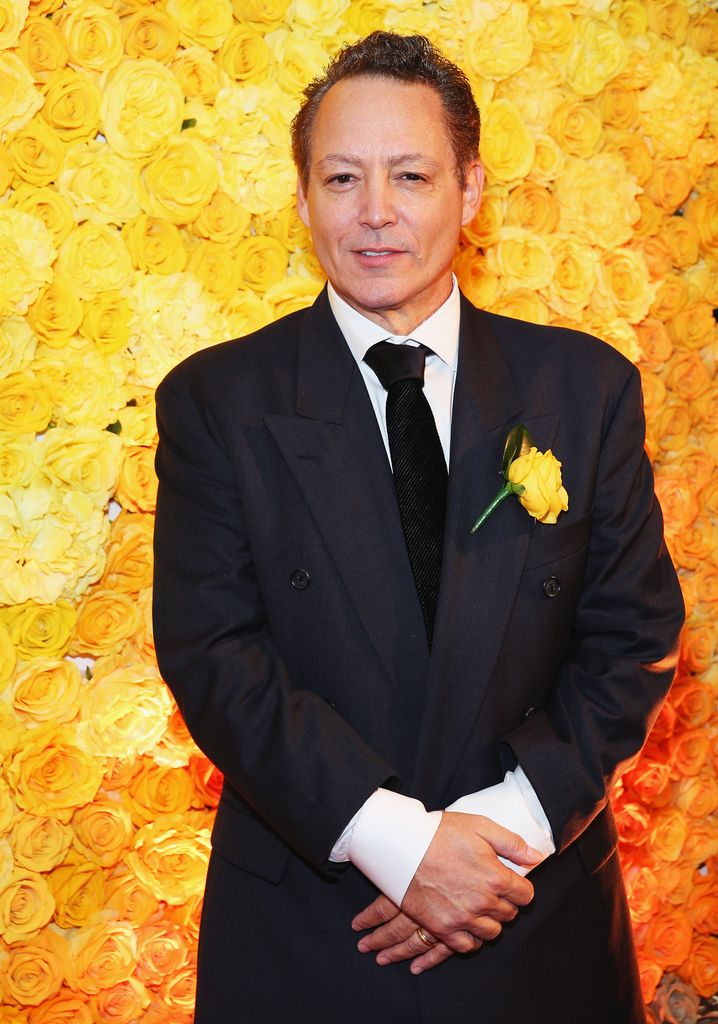 Dodd Darin porte un costume noir et une rose jaune sur son revers et se tient devant un mur de roses jaunes.