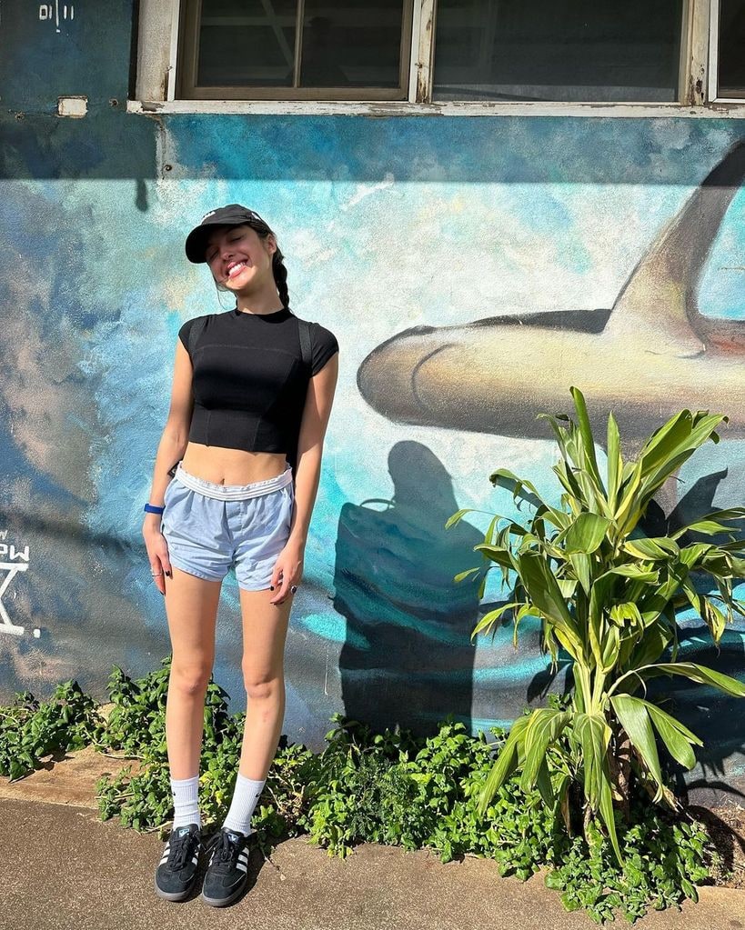 Olivia Rodrigo wearing denim shorts a black crop top and a baseball cap