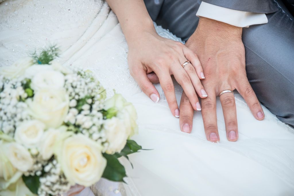 A bride and groom holding hands showing their wedding rings