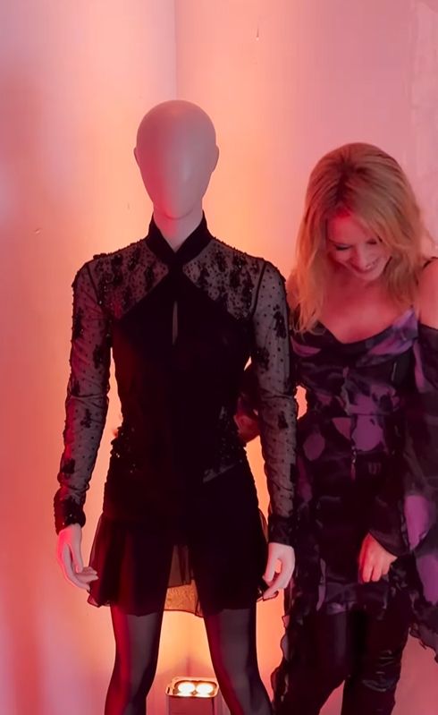 Kylie Minogue in a purple and black dress standing next to a mannequin
