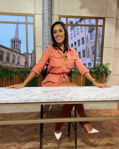 Janette Manrara behind a desk in salmon coloured mini dress