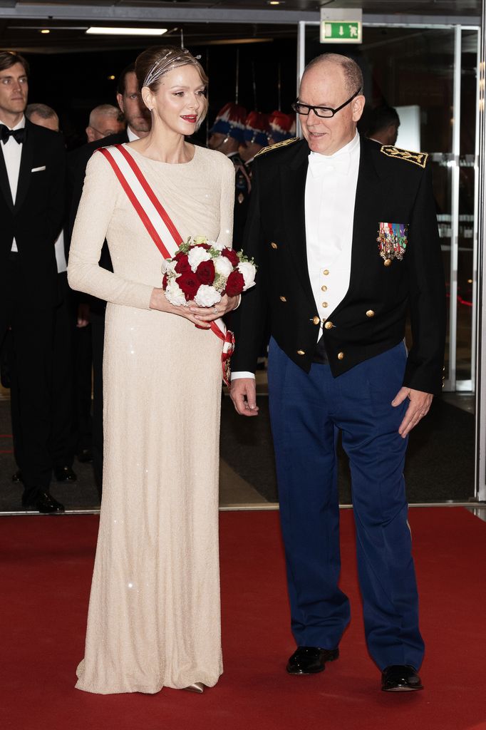 Princess Charlene in white dress and Prince Albert entering event on red carpet
