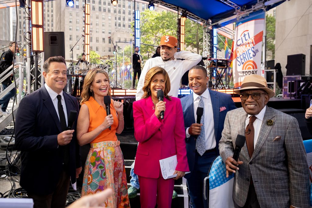 Hoda Kotb and Savannah Guthrie smiling while holding mics and hosting Today outside