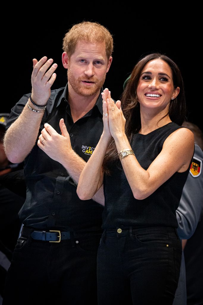 Prince Harry, Duke of Sussex and Meghan with hands up in black