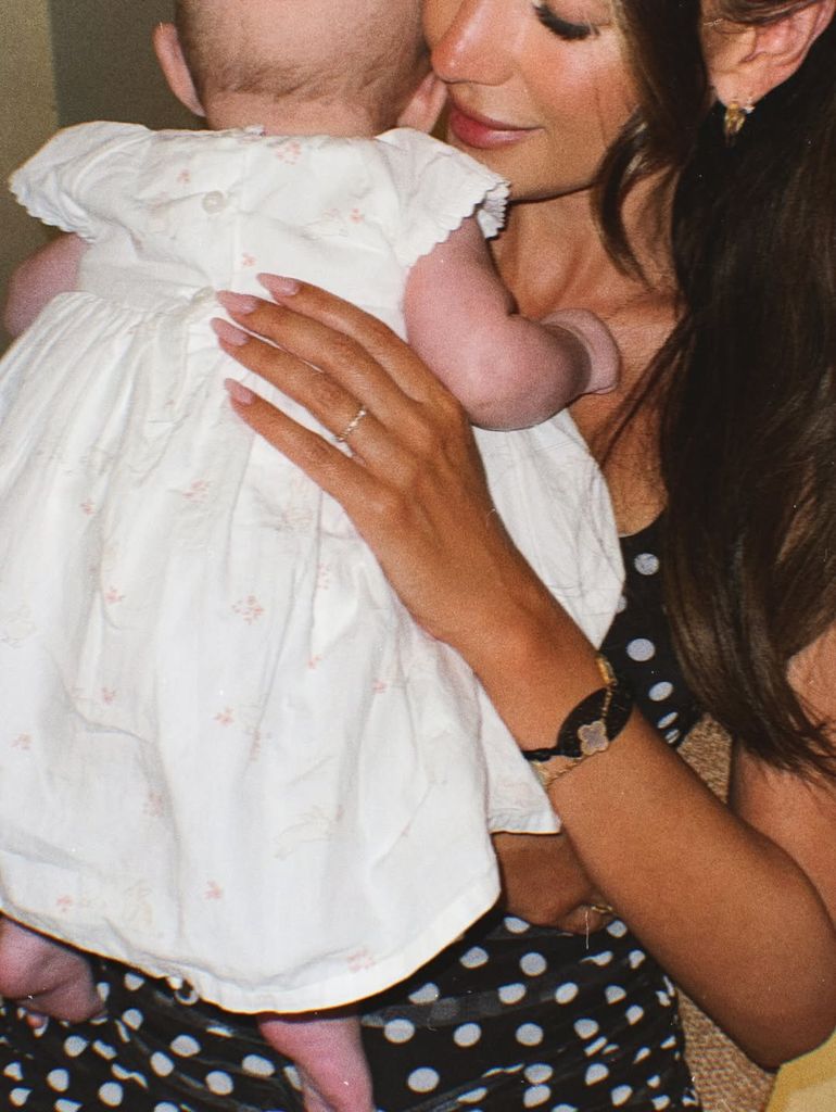 Michelle Keegan a Pola Dot River sosteniendo al bebé Palma que lleva ropa blanca