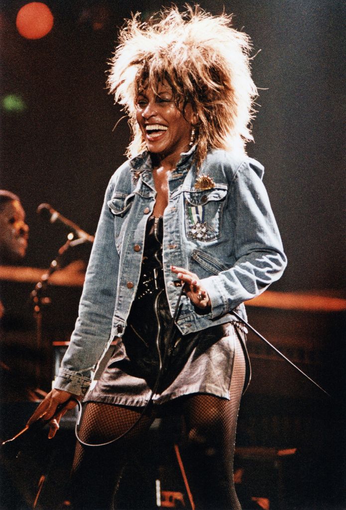 Tina Turner wearing a denim jacket and a leather zip-up mini dress