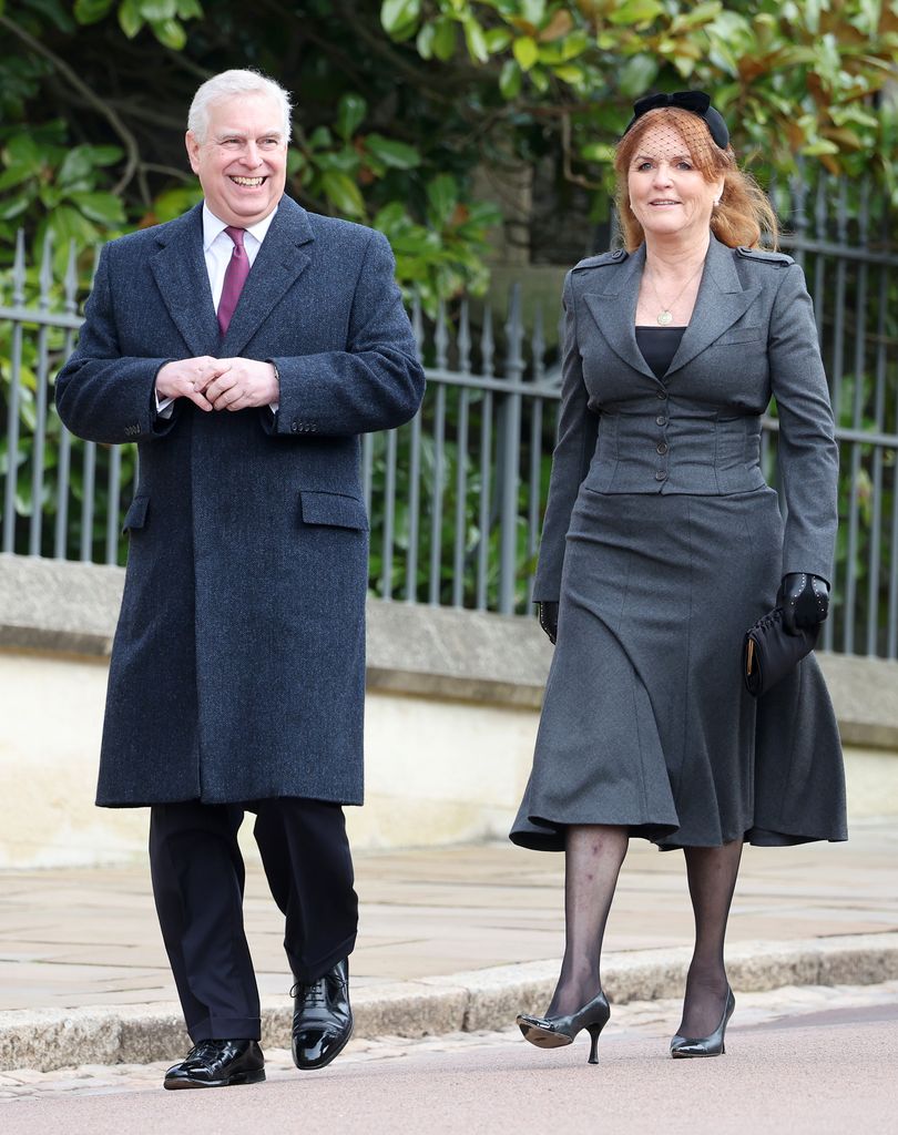 Andrew Mountbatten-Windsor, wearing a long black coat and trousers, laughs while walking next to Sarah Ferguson. She wears a grey waistcoat and skirt co-ord with tights and heels.