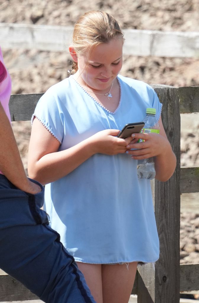 Mia Tindall texting in her phone wearing a baby blue tee