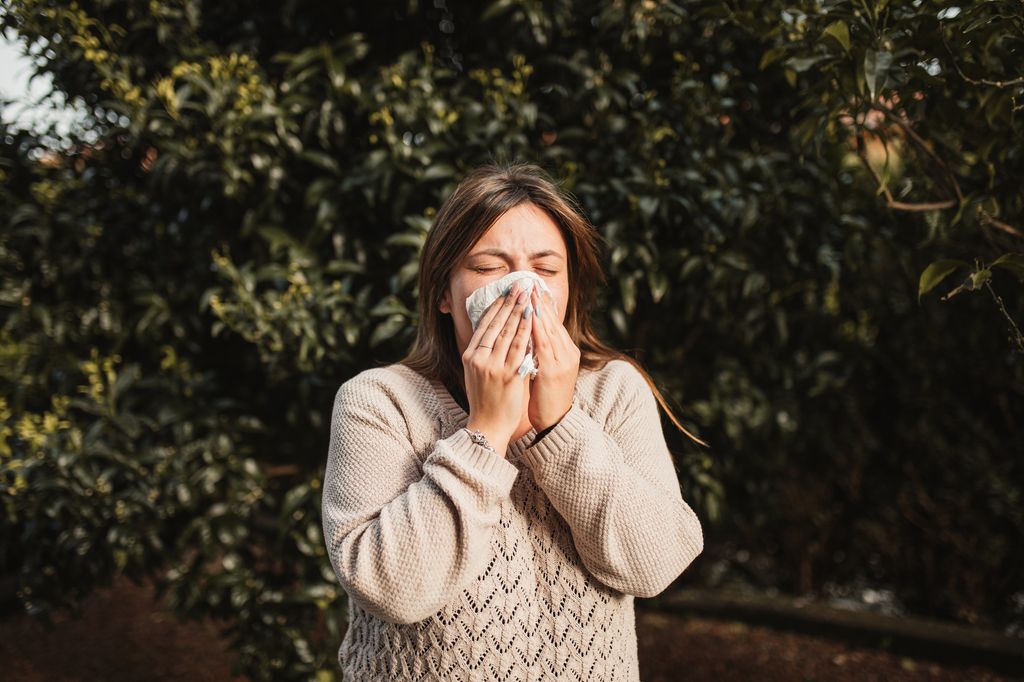 young woman sneezing wearing a jumper and she is outdoors 
