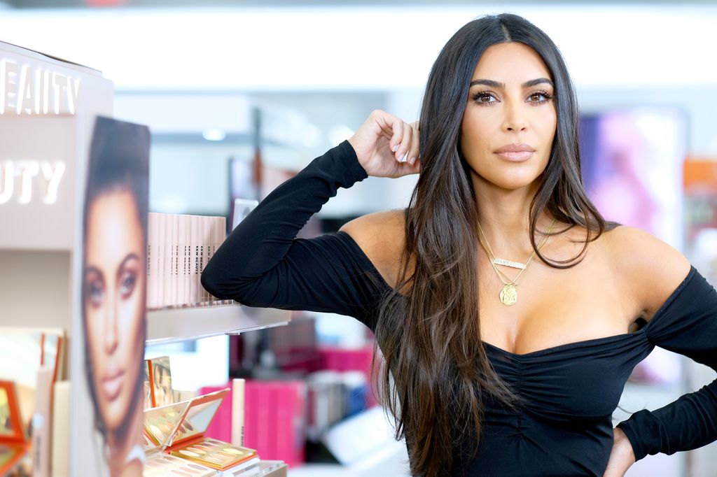 Kim Kardashian standing next to her KKW Beauty display in 2019