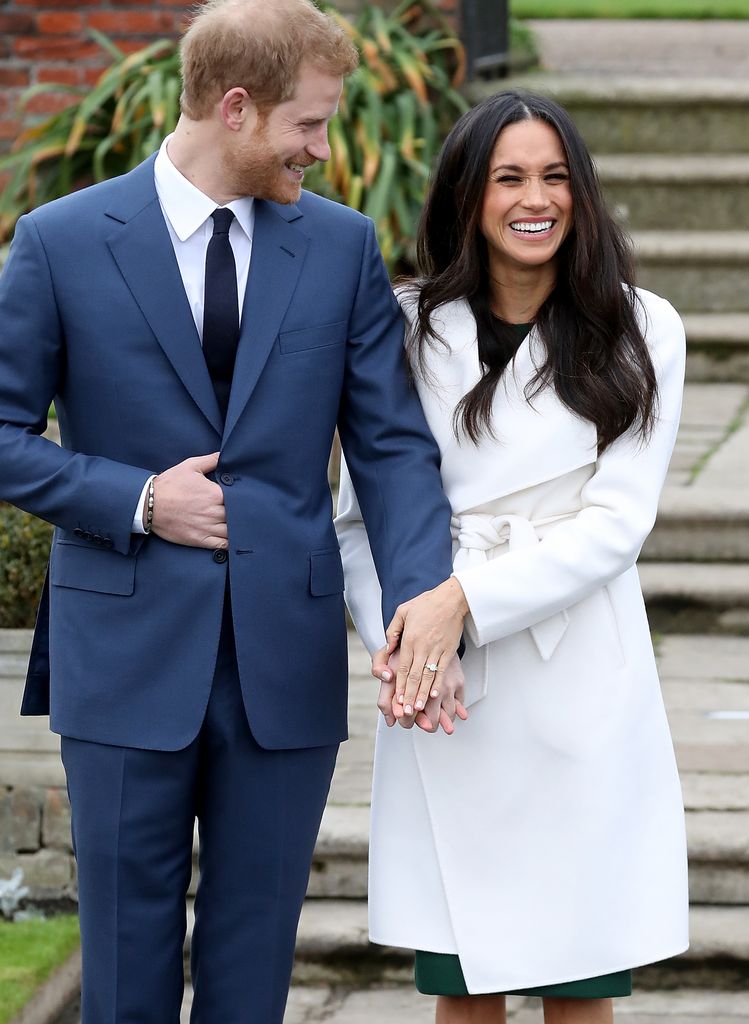 Príncipe Harry olha para Meghan Markle enquanto ela ri de jaleco branco