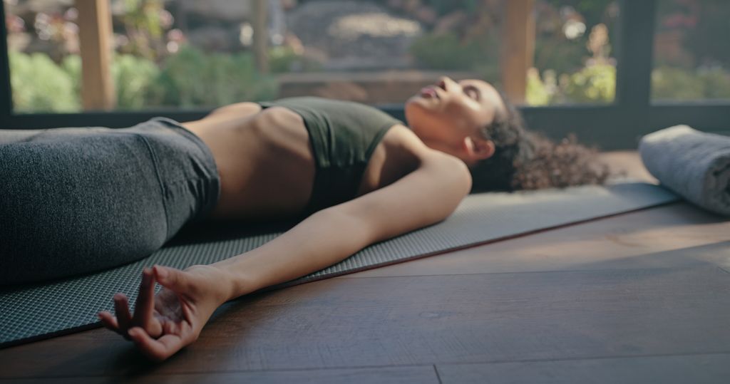 Meditation, yoga and peace hand of black woman on pilates studio floor for fitness and wellness. Rest, zen and peace practice of a young person sleeping on the home gym ground for balance and chakra