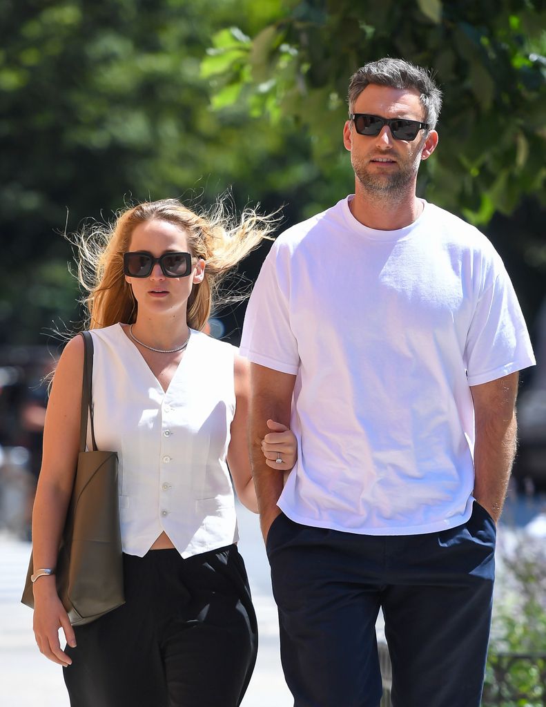 Jennifer Lawrence in a white waistcoat wearing sunglasses linking arms with Cooke Maroney in a white top and sunglasses