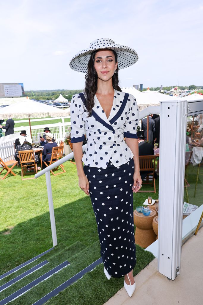 Ellie Evelyn Smith wears a fitted polka dot skirt suit with a large matching hat and white pointed heels at Royal Ascot.