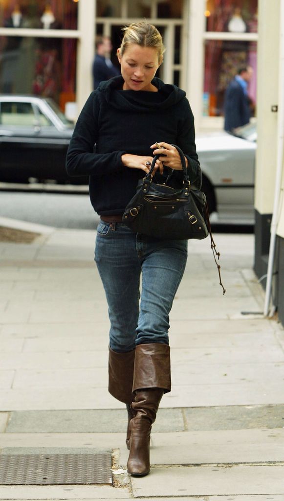 Kate Moss in brown boots, jeans, and black top holding bag