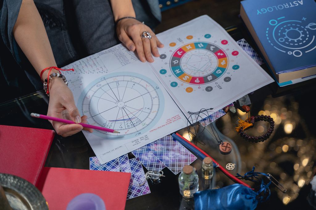 A female astrologer charts an astrology chart for a client while holding a pencil in one hand