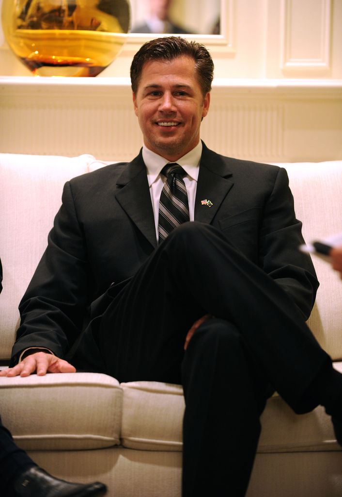 Doug Pitt sitting on a sofa in a black suit