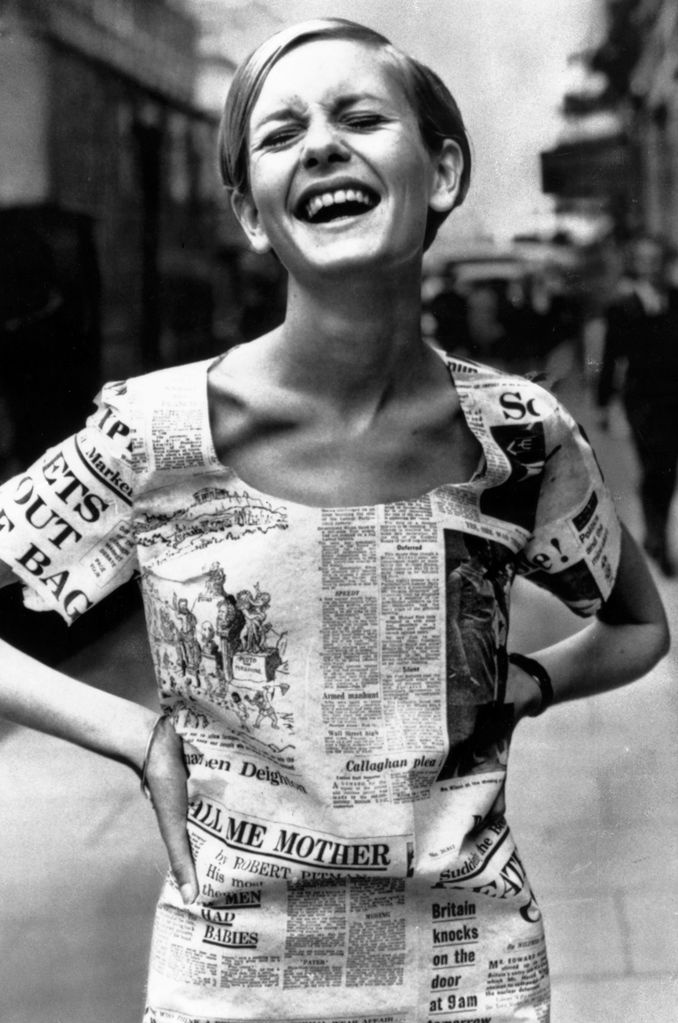 Twiggy embodies the mod spirit in a playful newspaper-printed dress. Her wide smile and carefree attitude represent the youthful exuberance of 1960s fashion. The minimalist makeup and pixie haircut complement the bold dress, which captures the era’s avant-garde approach to print and patterns.