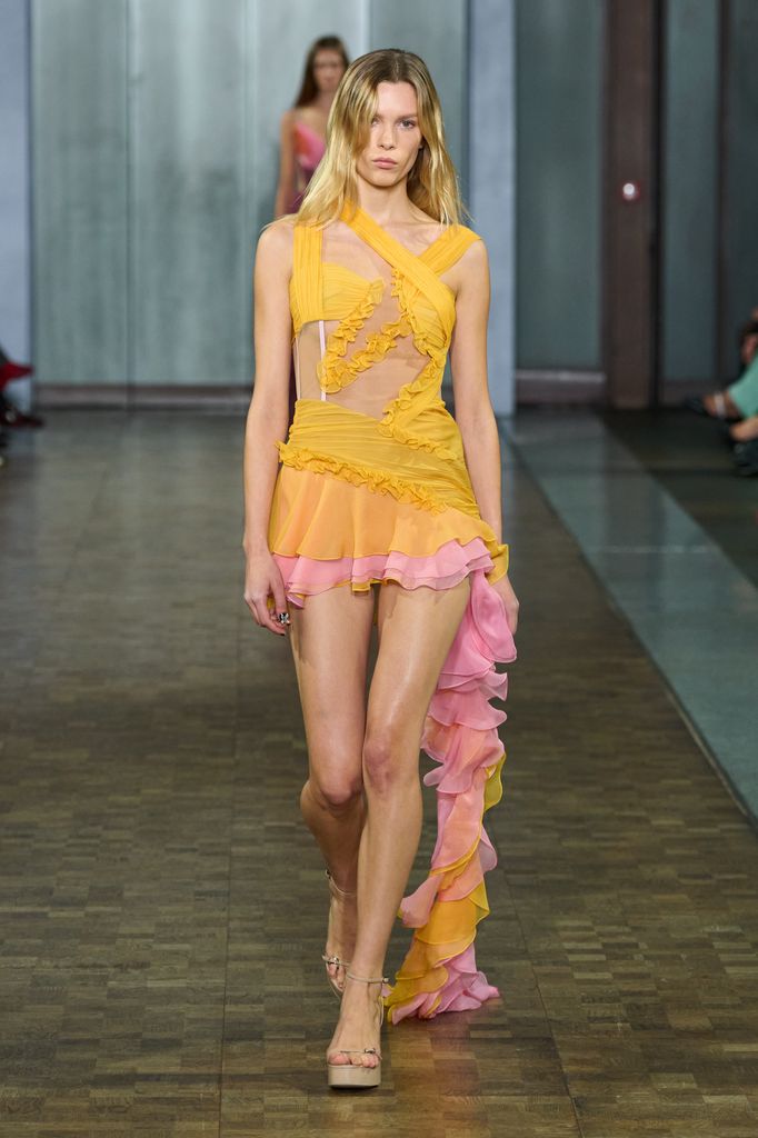 A model walks down the runway wearing a yellow orange and pink Y2K inspired mini dress