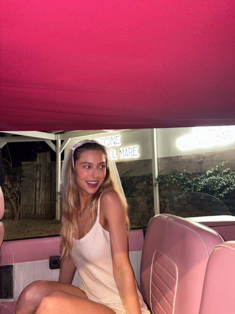 Eve Jobs in a white sparkly mini dress and veil in a pink car