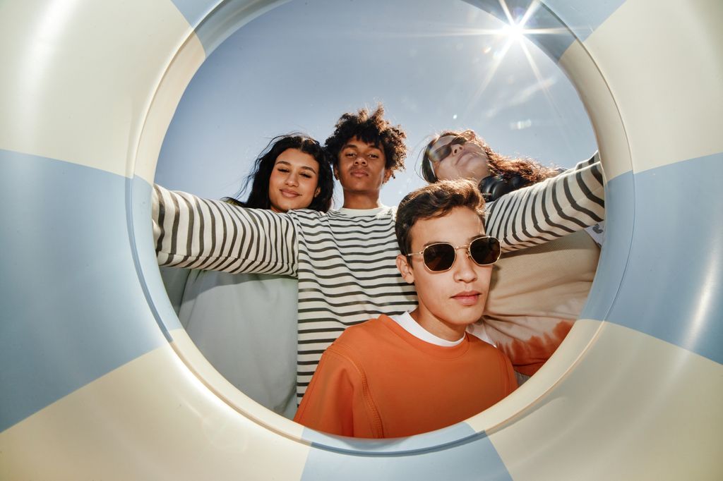  Four teenagers posing together holding a swimming tube in the sun at the beach.