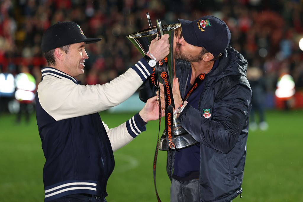 Ryan Reynolds and Rob McElhenney with the Vanarama National League Trophy as Wrexham celebrate promotion back to the English Football League during the Vanarama National League match between Wrexham and Boreham Wood at Racecourse Ground on April 22, 2023 