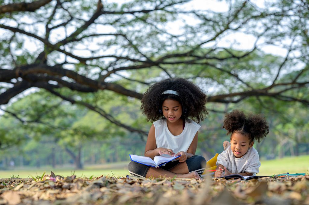 Girls reading a book and drawing in summer garden 