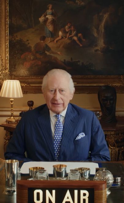 King Charles sitting behind an 'on air' sign at a desk