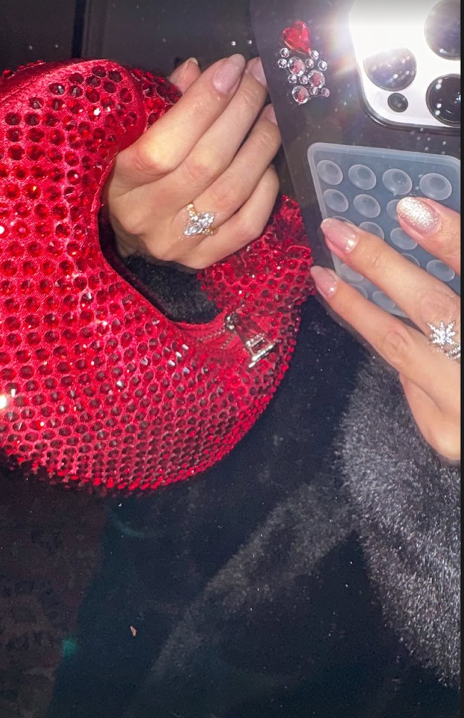 Selena Gomez holds a red rhinestone embellished bag, showcasing her engagement ring and glitter manicure