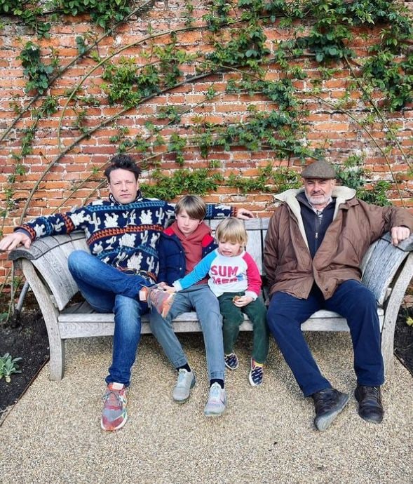 Jamie Oliver, his two sons and father sat on a bench