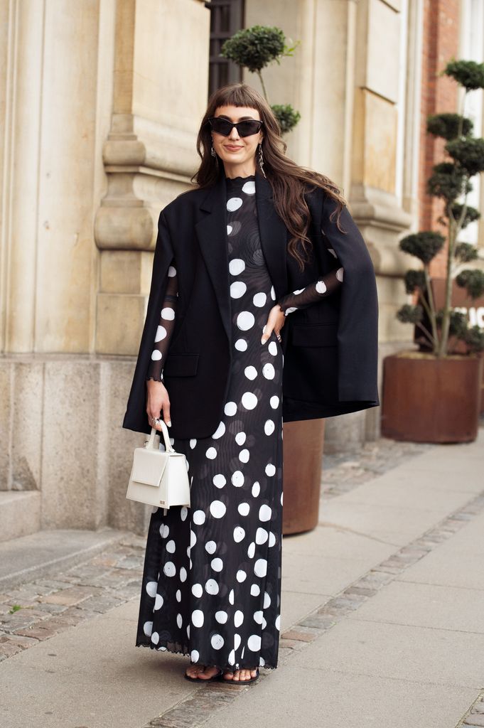 Mari Alexander wears black maxi dress with white circles or polka dots, white bag and black blazer outside Deadwood during Copenhagen Fashion Week 