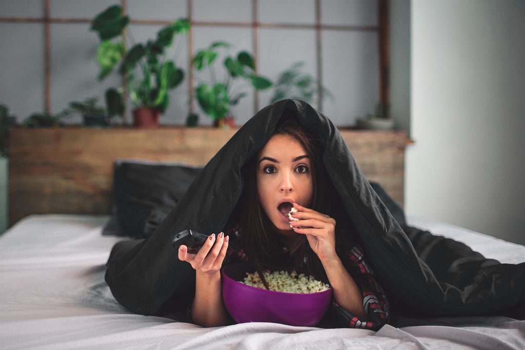 woman under blanket eating popcorn at home on weekend