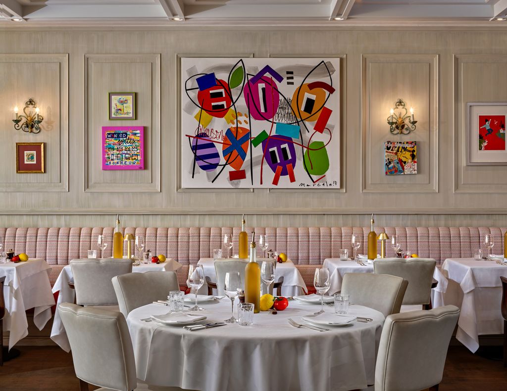 Tables and chairs in a restaurant with white cloth tables and colourful artwork on the walls