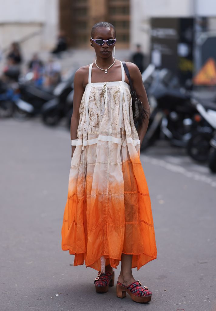Guest is seen outside Zimmermann show wearing lilac Oakley sunnies, silver chain, white and orange ombre colored dress,  beige hairy Fendi Baguette handbag and red checkered clogs with crystal details