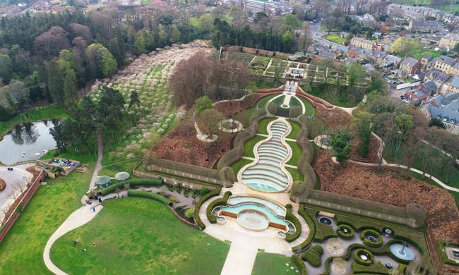 a photo taken from birds eye view of a huge garden featuring decorative ponds and manicured lawns surrounded by forest and landscaped areas of scrubbery