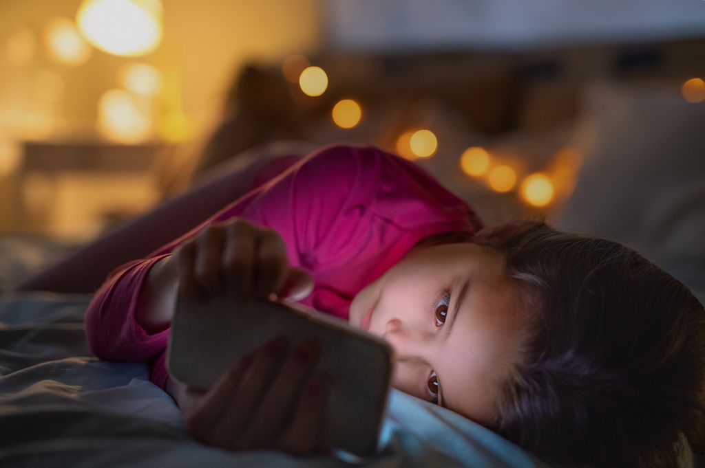 Small girl indoors on bed at night, using telephone.