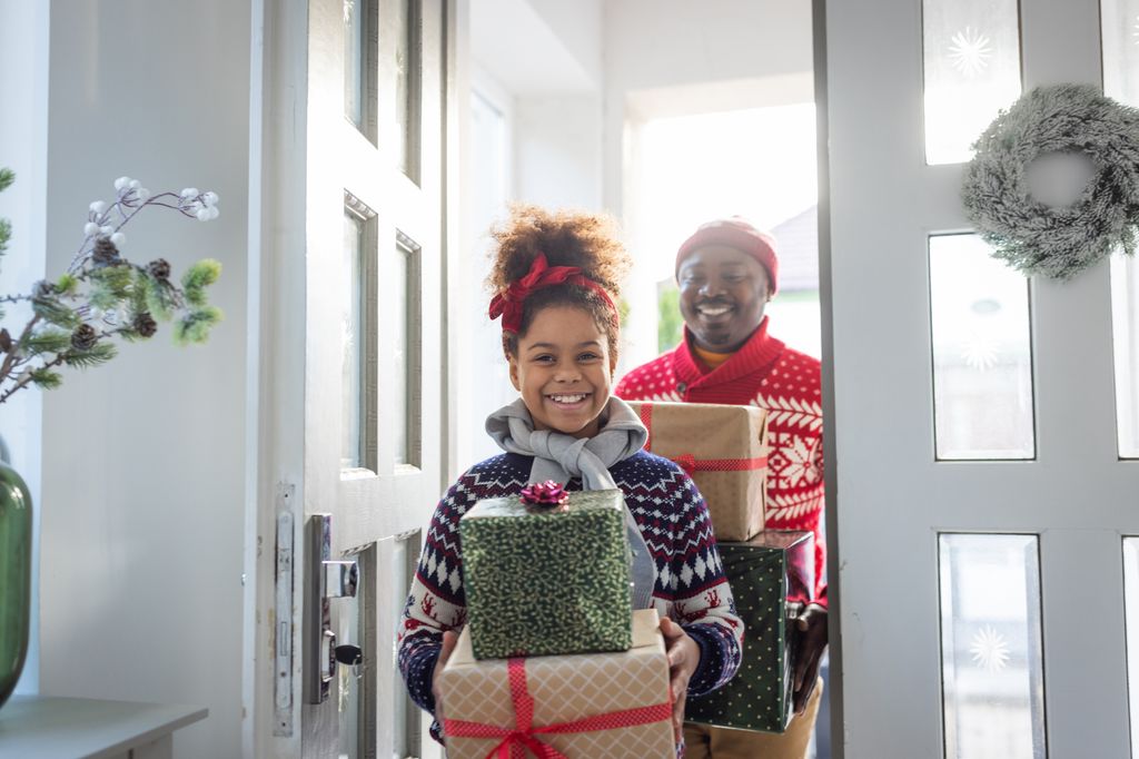 Father and daughter entering in home and holding pile of Christmas gifts 