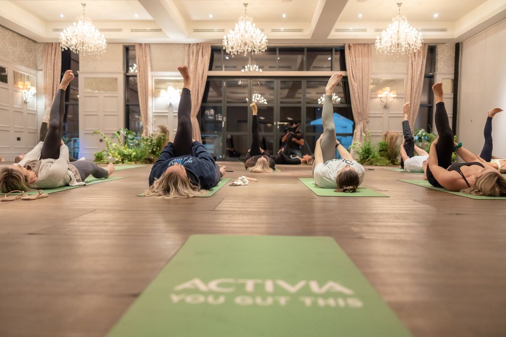 Class of people doing yoga on green mats with chandeliers overhead