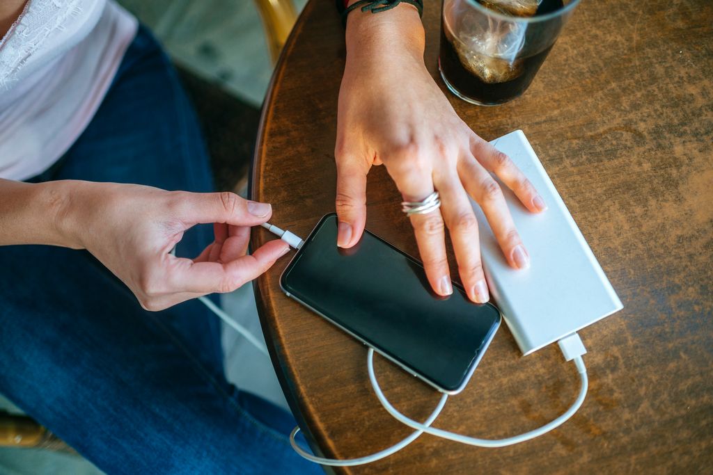 Close-up of Woman's hands plugging a mobile phone into apower bank in a bar