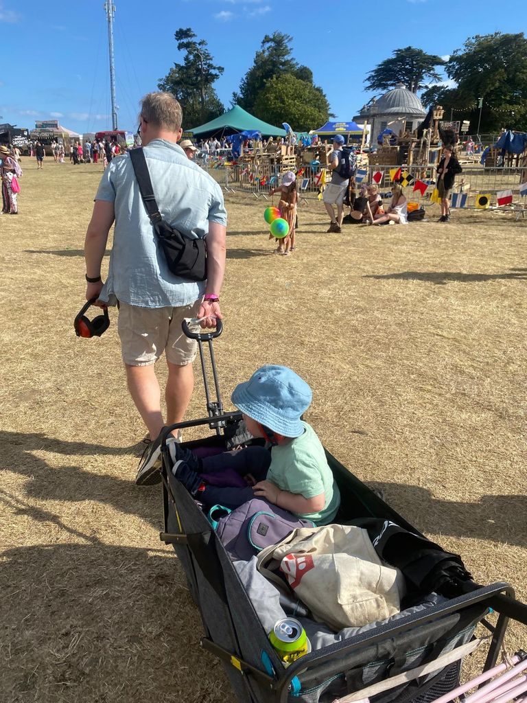 Man in blue shirt and shorts pulling a festival wagon containing a little boy