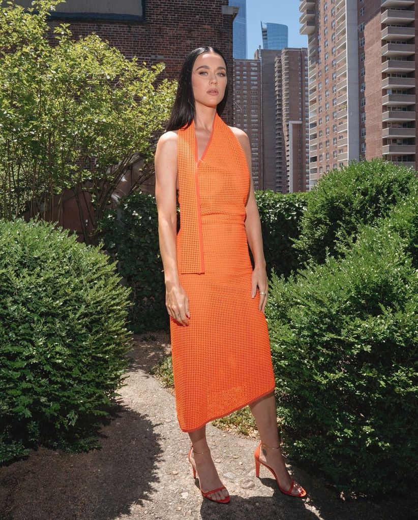 Katy Perry está em um parque em Nova York usando um vestido laranja