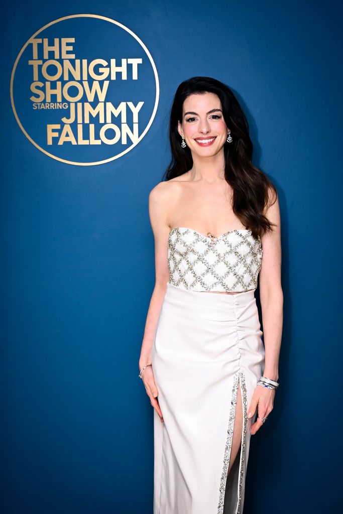 Anne Hathaway in white in front of Jimmy Fallon sign