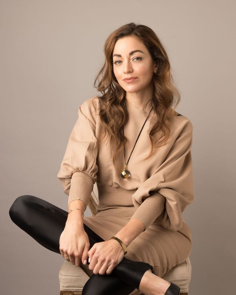 woman smiling in a camel coloured top and black leggings 